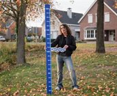 Persoon straat op de foto met fysieke waterpeilstok voor huis.